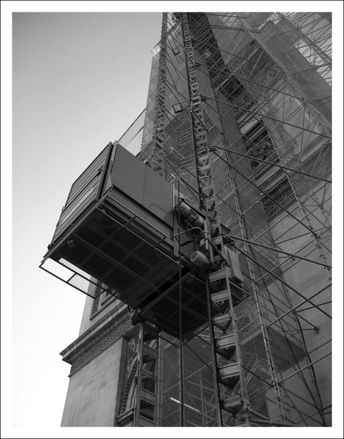 Ascenseur de chantier contre l’arc de triomphe, noter l’amarrage et les plates-formes d’accès (Doc. Skyacces).
			